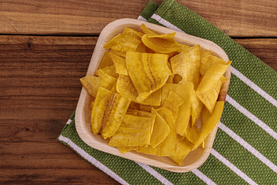 Crispy Banana Chips. Fried or baked sliced banana. Top view of typical traditional dish of Latin American gastronomy called Chifles or fried tostones on a wooden table. Roasted banana. Snack.
