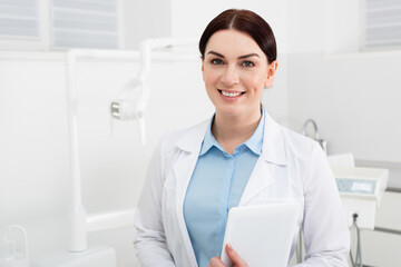 portrait of smiling dentist holding tablet and looking at camera in dental clinic.