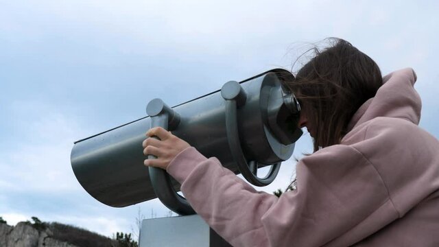 Woman traveler using Tower Optical Viewer to explore city buildings on the horizon, young girl exploring the city with binoculars