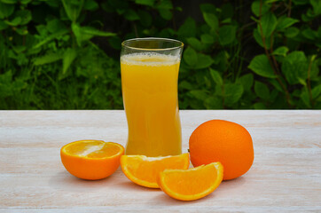 refreshing fruit summer cocktail or juice in a glass glass, cooling orange drink with a slice of pineapple outdoors on wooden table on green leaves background, eco friendly and organic concept
