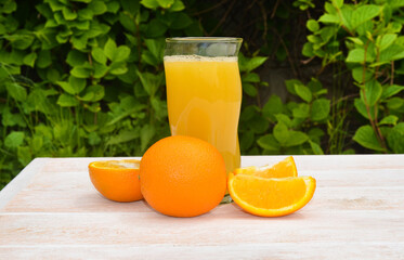 refreshing fruit summer cocktail or juice in a glass glass, cooling orange drink with a slice of pineapple outdoors on wooden table on green leaves background, eco friendly and organic concept