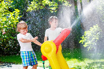 Two little kids boys playing with a garden hose water sprinkler