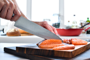 Hand slicing fresh raw salmon fillet steaks on a cutting board in the kitchen