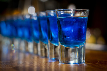 Selective focus shot of blue drink in shot glasses on a wooden bar counter