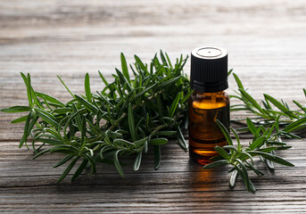 A bunch of fresh rosemary and a bottle of essential oil placed on a wooden background.
