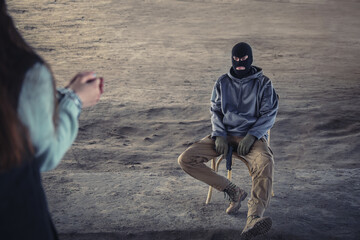 Male terrorist sitting on chair against female hostage outdoors