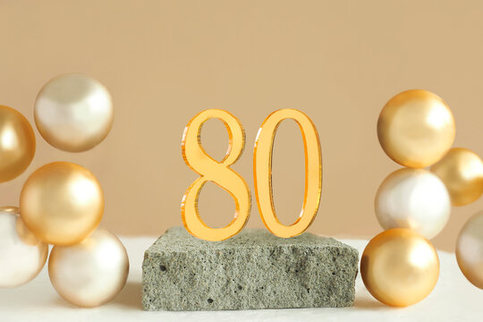 Number 80 on a concrete podium and volumetric golden balls on a beige background. Copy space..