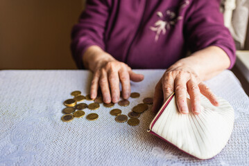 Old woman sitting miserably at home and counting remaining coins from the pension in her wallet after paying the bills.