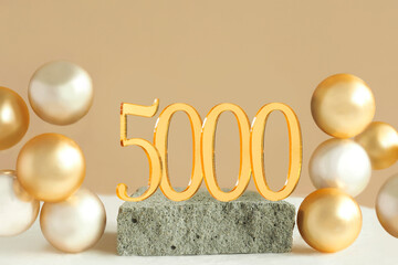 Number 5000 on a concrete podium and volumetric golden balls on a beige background. Copy space..
