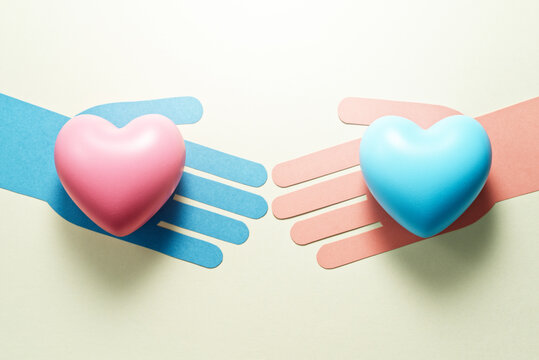 Concept image of transgender. Blue hand holding pink heart and pink hand holding blue heart.