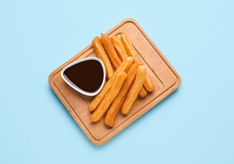 Board with tasty churros and melted chocolate sauce on color background