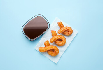 Parchment with tasty churros and melted chocolate sauce on color background