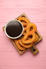 Board with tasty churros and melted chocolate sauce on color wooden background