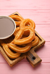 Board with tasty churros and melted chocolate sauce on color wooden background, closeup