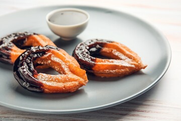 Plate with tasty churros dipped in chocolate on light wooden background, closeup