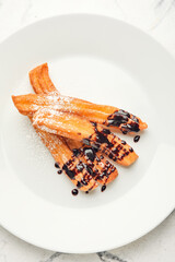 Plate with tasty churros dipped in chocolate on light background
