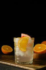 Glass of tasty cold lemonade and citrus fruits on dark background