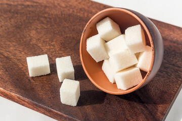 In a clay bowl, lumpy sweet white sugar on a wooden board. 