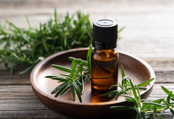 A bunch of fresh rosemary and a bottle of essential oil placed on a wooden background.