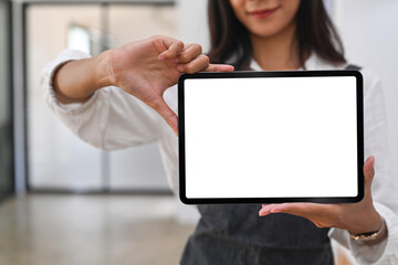 Close up view of happy woman barista showing digital tablet with blank screen while standing in coffee shop.