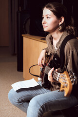 young woman playing bass guitar and reading chord notes at band rehearsal. vertical size. studio sound check. woman looking aside