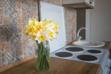 A bouquet of many daffodils in a glass vase on the kitchen table on background white kitchen. Design concept.
