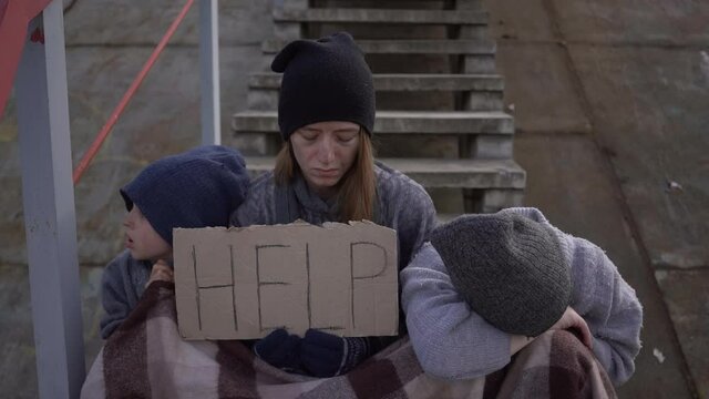 homeless mother with children with a sign Help on the stairs in an abandoned place homeless children with dirty face and hands needs help. Social problems, Homelessness, refugee problems, fleeing war