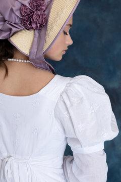 A young Regency woman wearing a white muslin dress and a straw bonnet
