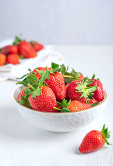 Refreshing organic garden strawberries with bright red color, juicy texture, and sweetness, source of vitamin C, manganese and dietary minerals served in bowl on white wooden table. Vertical image
