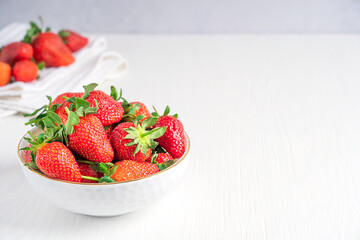 Fresh organic scented garden strawberries with bright red color, juicy texture and sweetness, source of vitamin C and dietary minerals served in bowl on white wooden background. Image with copy space