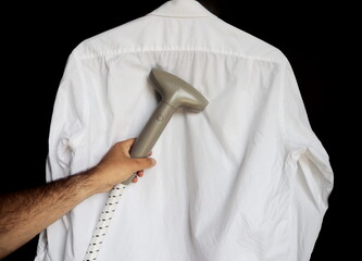Man ironing shirt with garment steamer  - obrazy, fototapety, plakaty