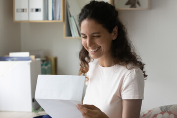 Smiling sincere millennial woman holding paper correspondence, reading letter with good news, feeling excited of getting bank loan approvement notification, taxes refund, university admission notice.