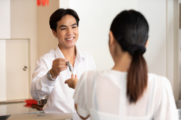 male receptionist or hotel front desk smiling and giving keycard to a customer