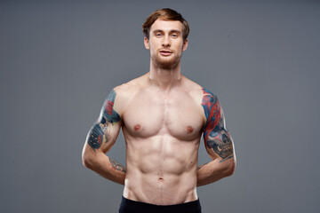 sporty man with tattoos on his arms pumped up press macho gray background