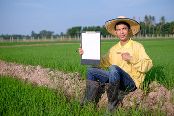 Asian farmers wear yellow shirts sitting and show paper board at the green farm. Image for presentation.