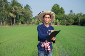 Asian farmer man wears traditional costume standing and writing paper board at green