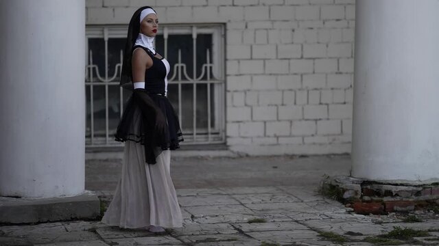 sexy lady is wearing erotic suit of catholic nun, woman is walking near old monastery