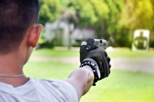 Automatic black 9mm pistol holding in hand aming to the shooting target ahead, concept for practicing and training pistol to protect oneself from mafias, gangster and robber selective focus on pistol.