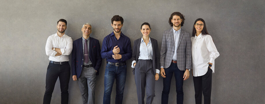 Team of happy satisfied business people standing leaning on grey concrete wall. Banner with group portrait of successful stylish business professionals, entrepreneurs, colleagues, company coworkers