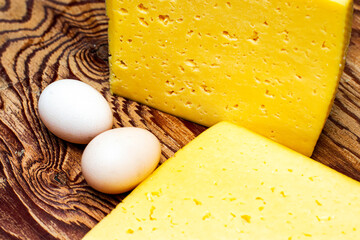 two large pieces of cheese and two chicken eggs on a wooden surface