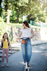 Obraz premium Mother and daughter in the park. Woman riding push scooter.