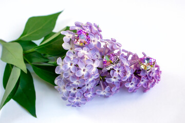 three lilac triangular crystals lie on a blossoming branch of lilac on a white table