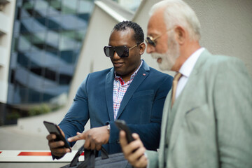 Naklejka na ściany i meble Two business men outdoors. Using smart phones.