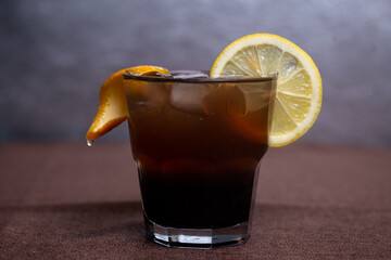 cold alcoholic brown cocktail with ice and lemon.