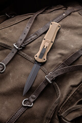 Modern folding knife on a rough canvas backpack. Melee weapons for self-defense and survival. A pocket knife on a rough dark back