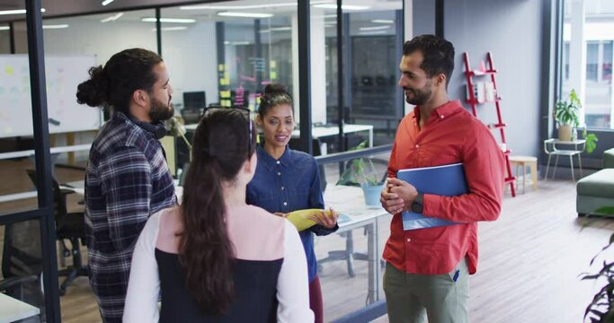 Diverse group of work colleagues standing holding documents and talking