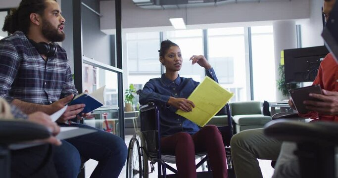 Mixed race businesswoman sitting in wheelchair discussing with diverse group of colleagues