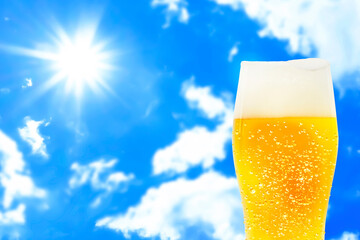 Image of a glass of beer with a blue sky and sun background and dripping foam.