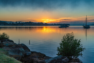 Sunrise waterscape with boats, light cloud and fog