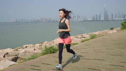 young asian woman jogging exercising by the sea with city background